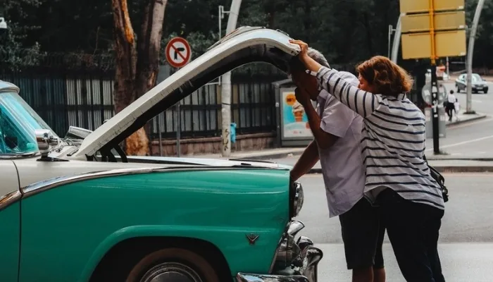 Dos personas revisando un carro usado en una calle concurrida de día