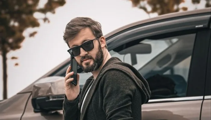 Vendedor de un carro usado hablando por teléfono junto al vehículo